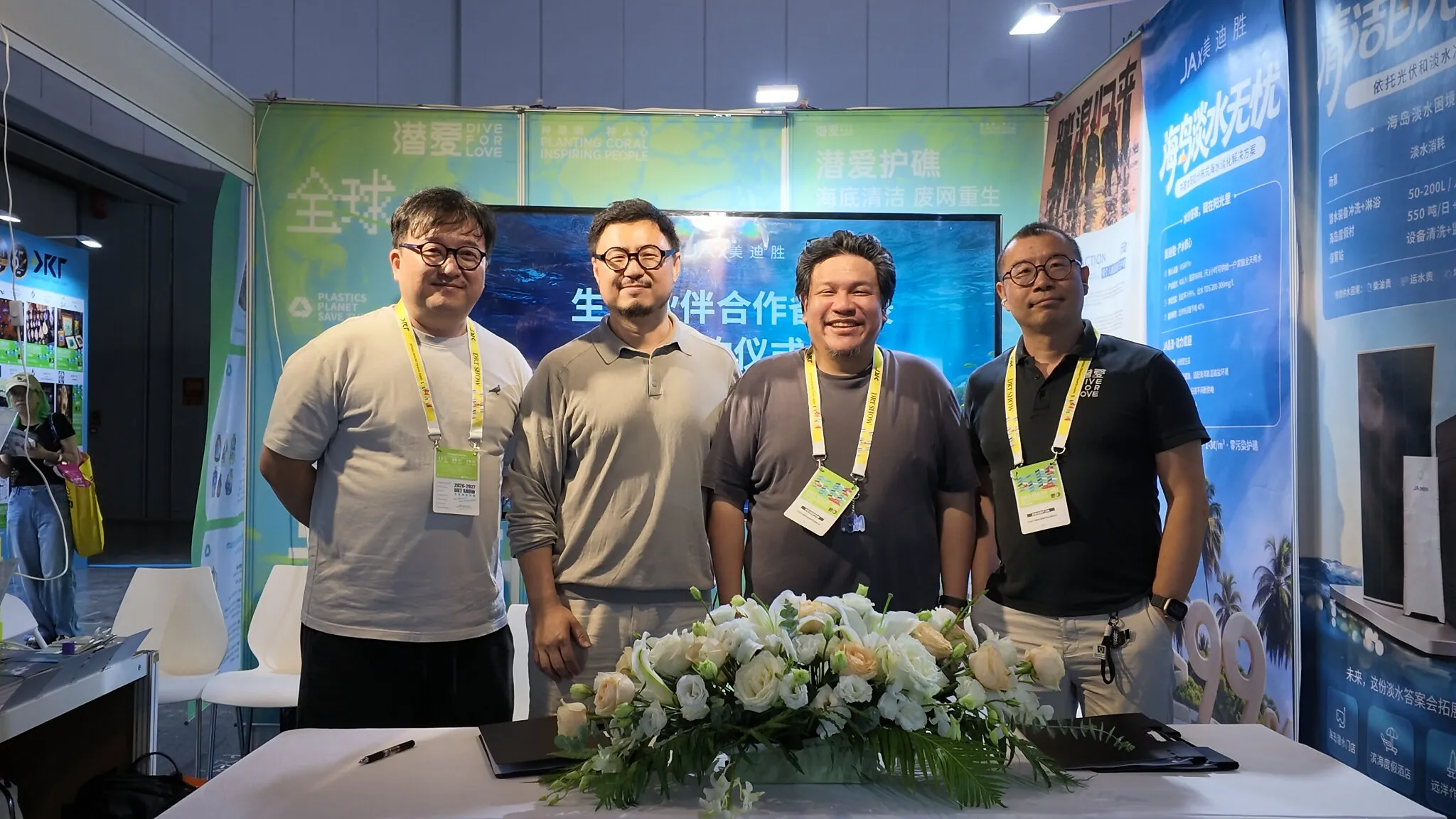 Four people stand behind a flower-covered table at an exhibition booth.