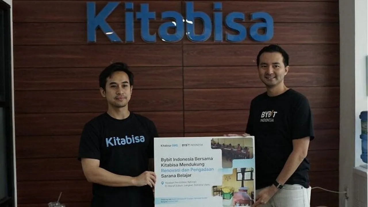 Two people hold a donation poster beneath a Kitabisa sign.