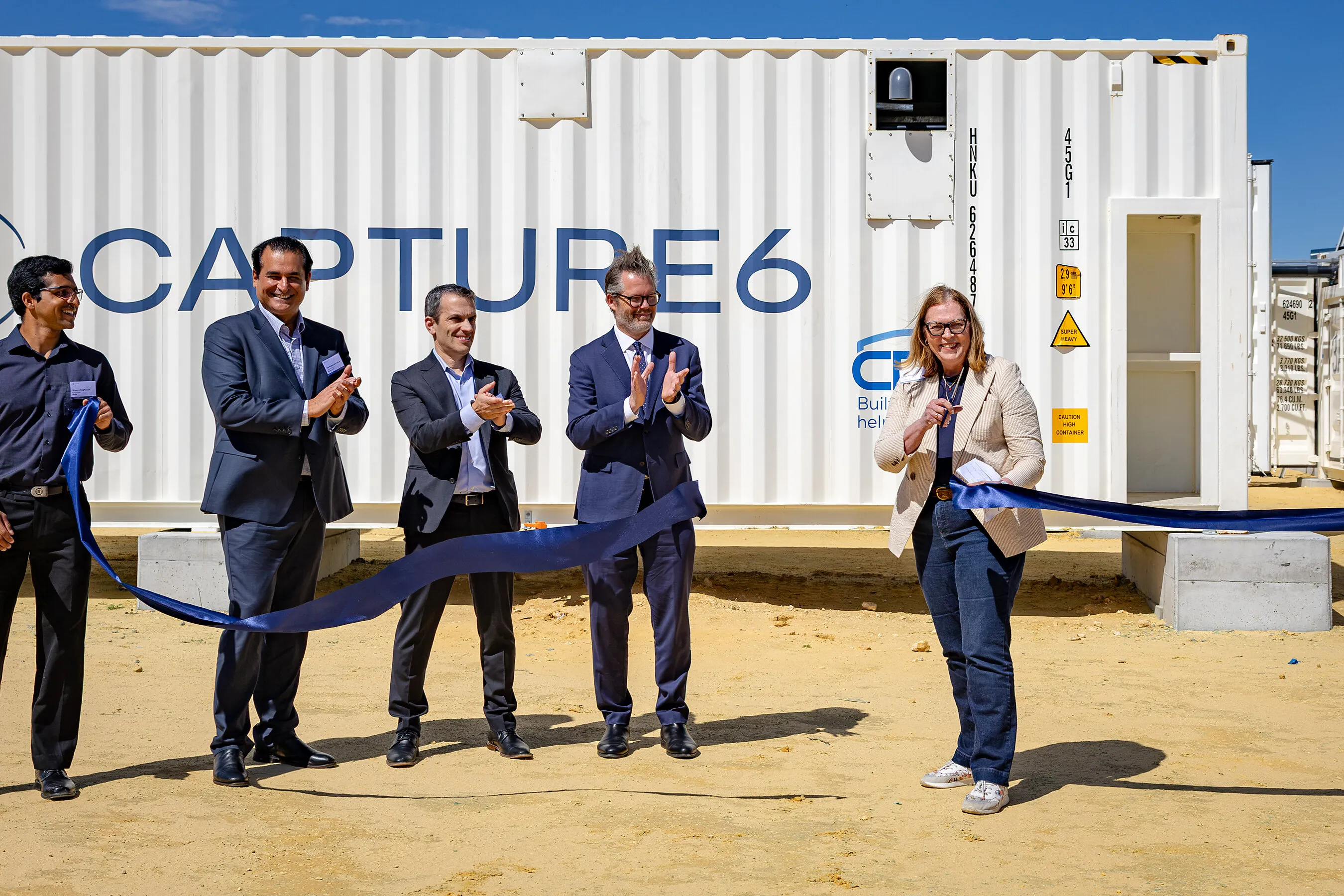 Five people at a ribbon-cutting in front of a Capture6 shipping-container facility.