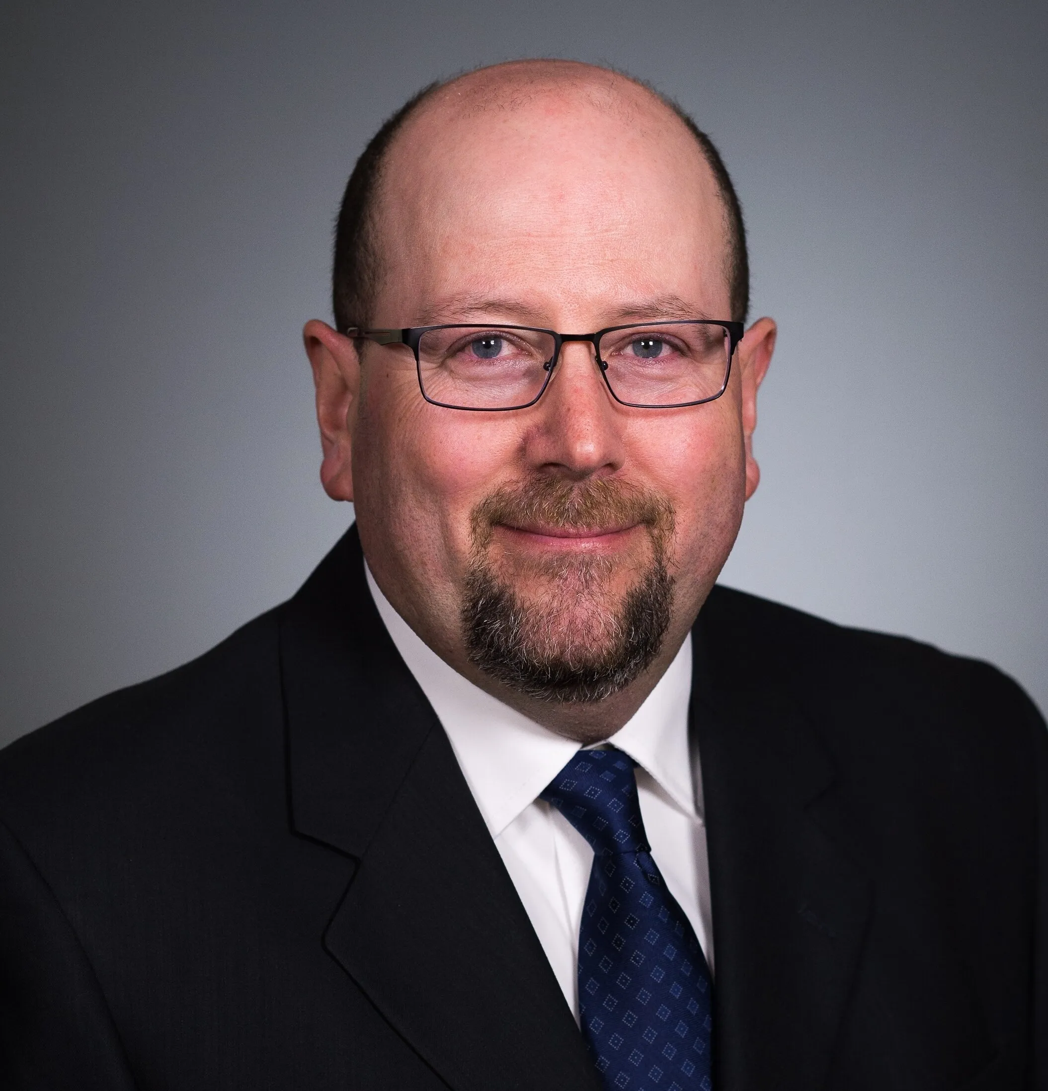 David Forcinito in glasses, a dark suit and blue tie against a gray background.