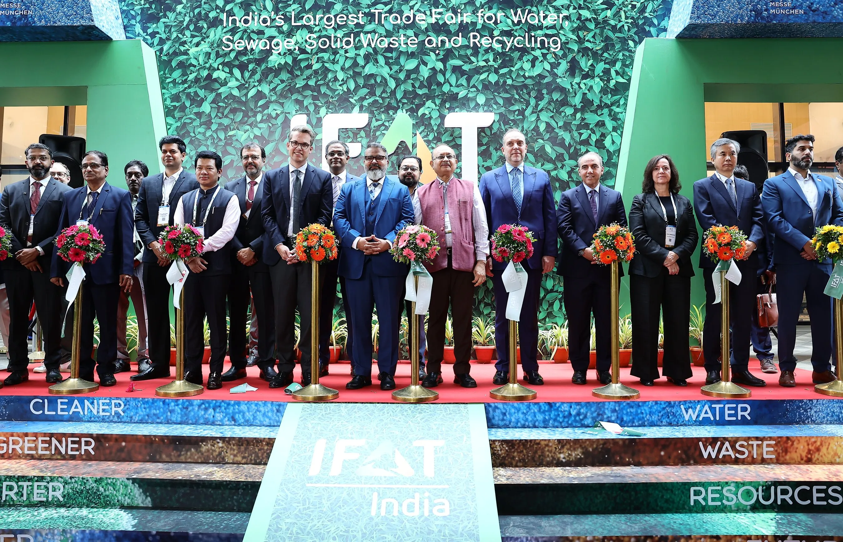 A group stands on the IFAT India stage behind bouquets on stands, beneath a sewage, waste and recycling sign.