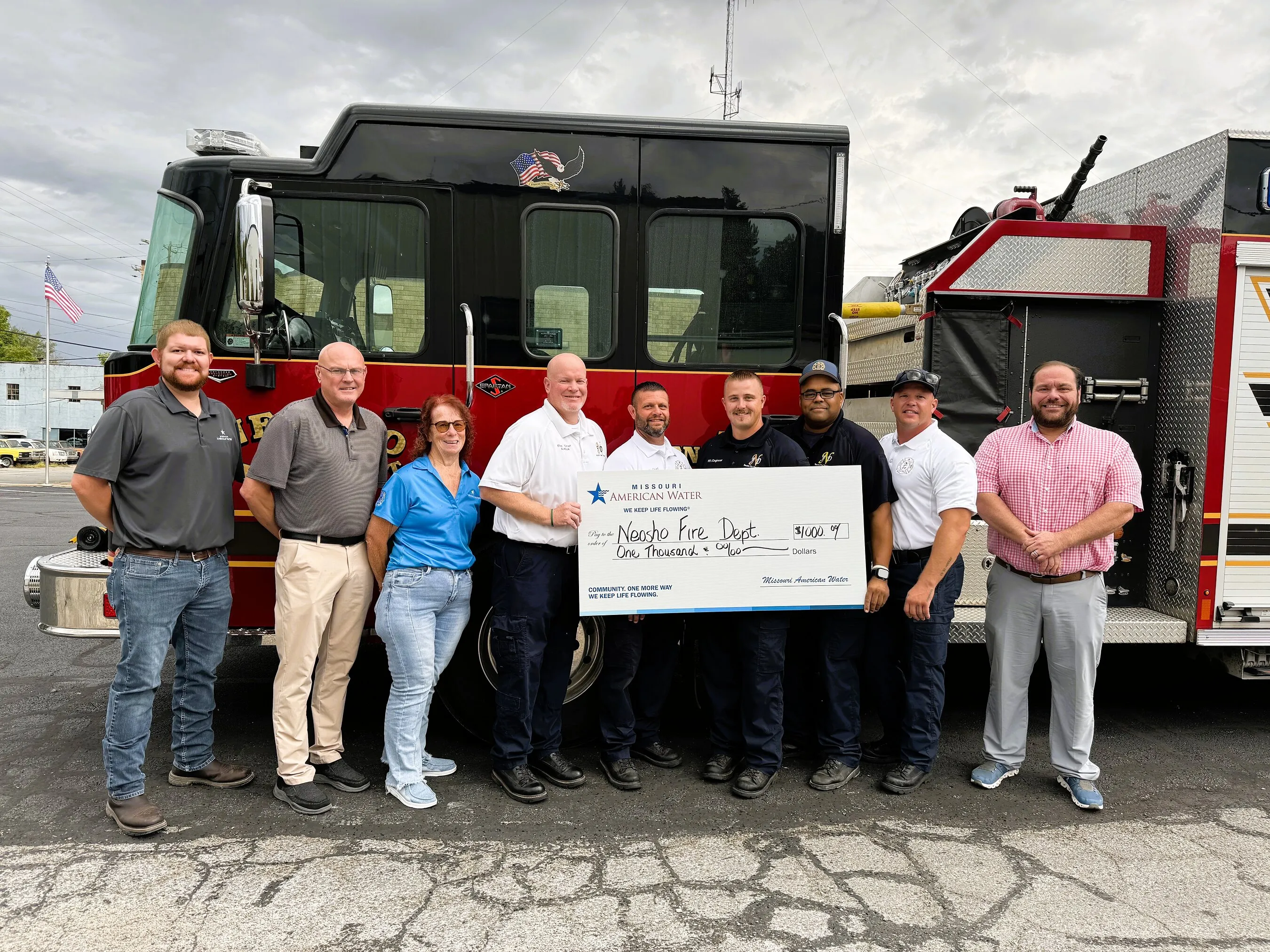 Missouri American Water employees and Neosho Fire Department staff hold a grant check in front of a fire truck.