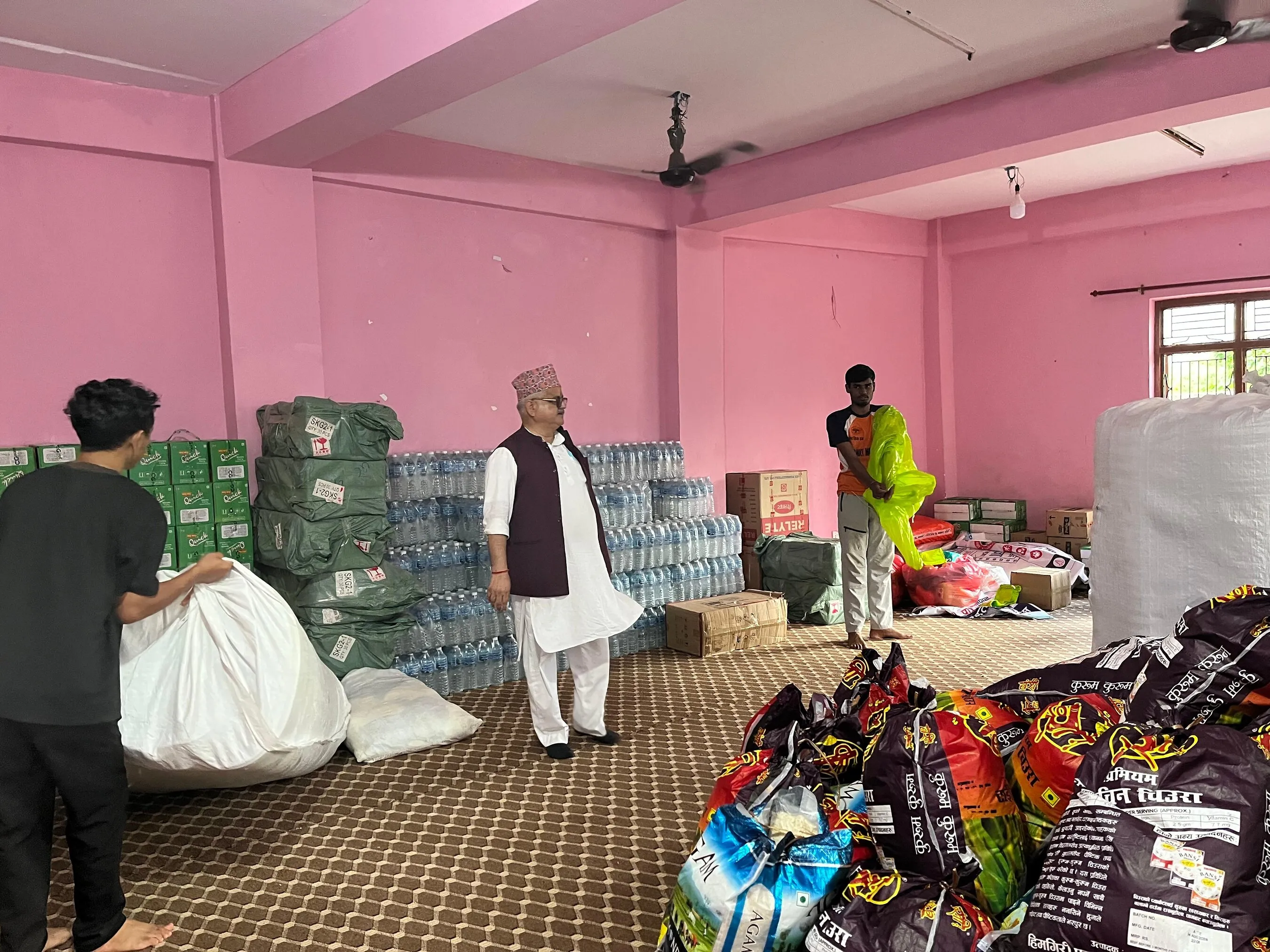Sewa volunteers sort relief supplies, including bottled water, sacks and boxed goods, in a storeroom.