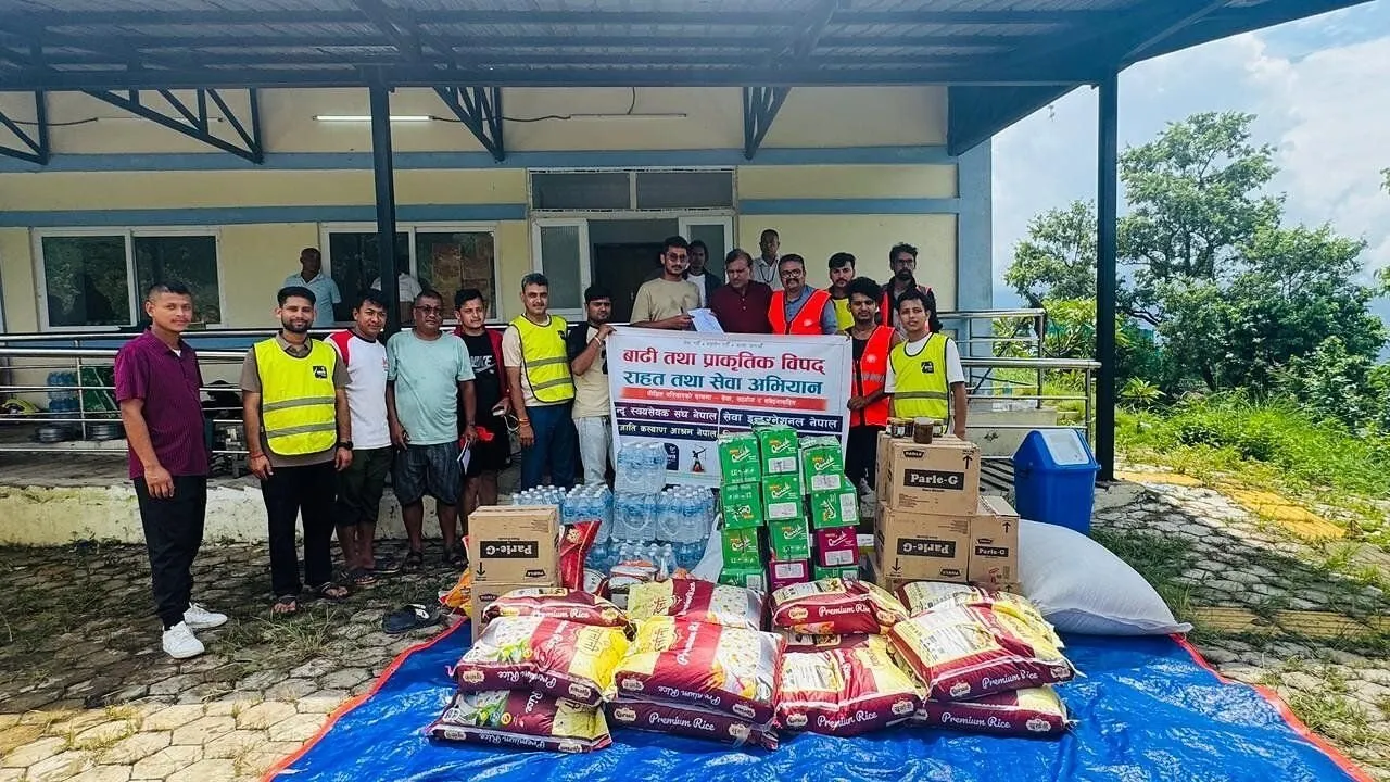 Volunteers stand behind rice, water, biscuits and boxed relief supplies on a blue tarp.