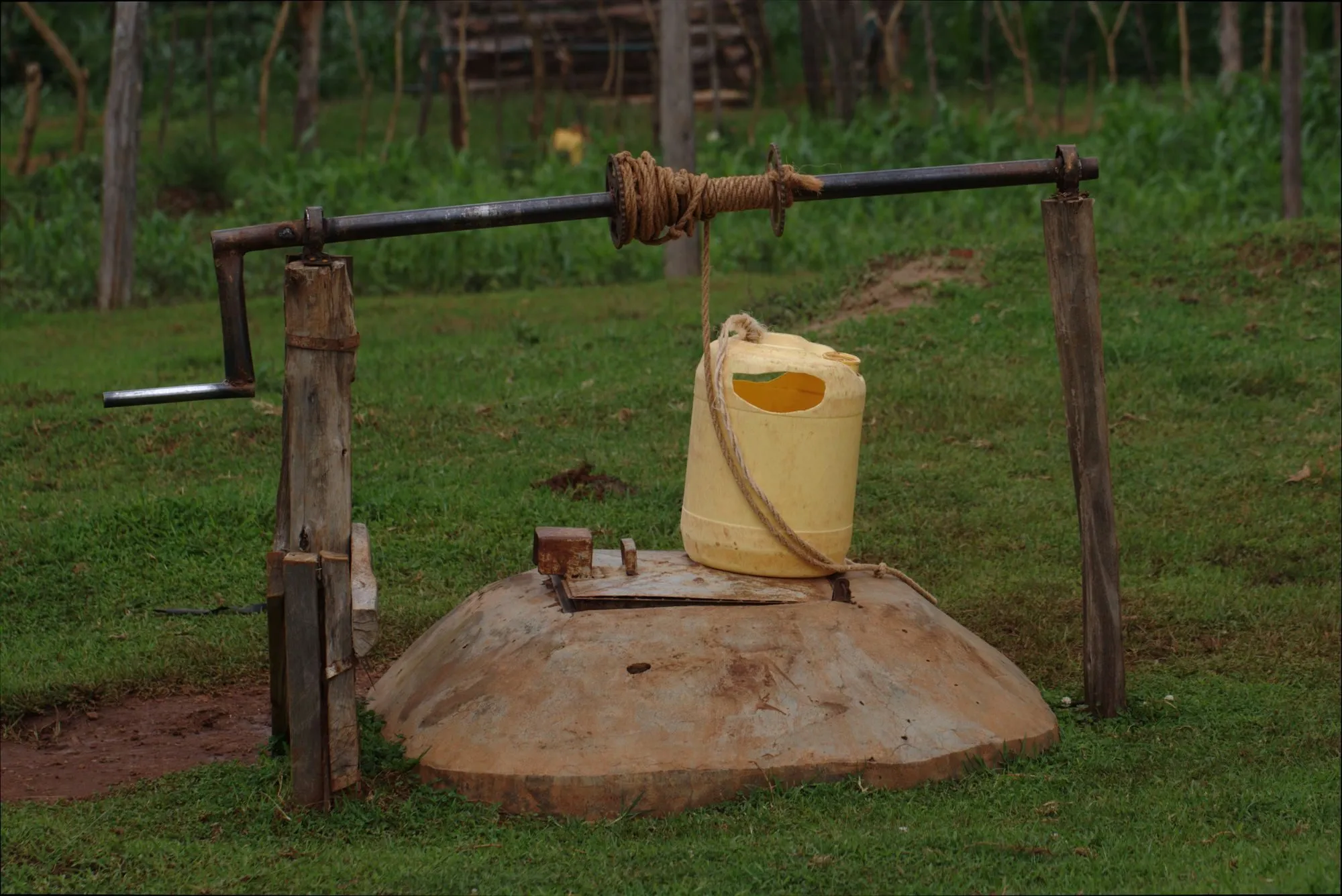 A hand-dug well with a rope winch and a yellow water container in rural Kitale, Kenya