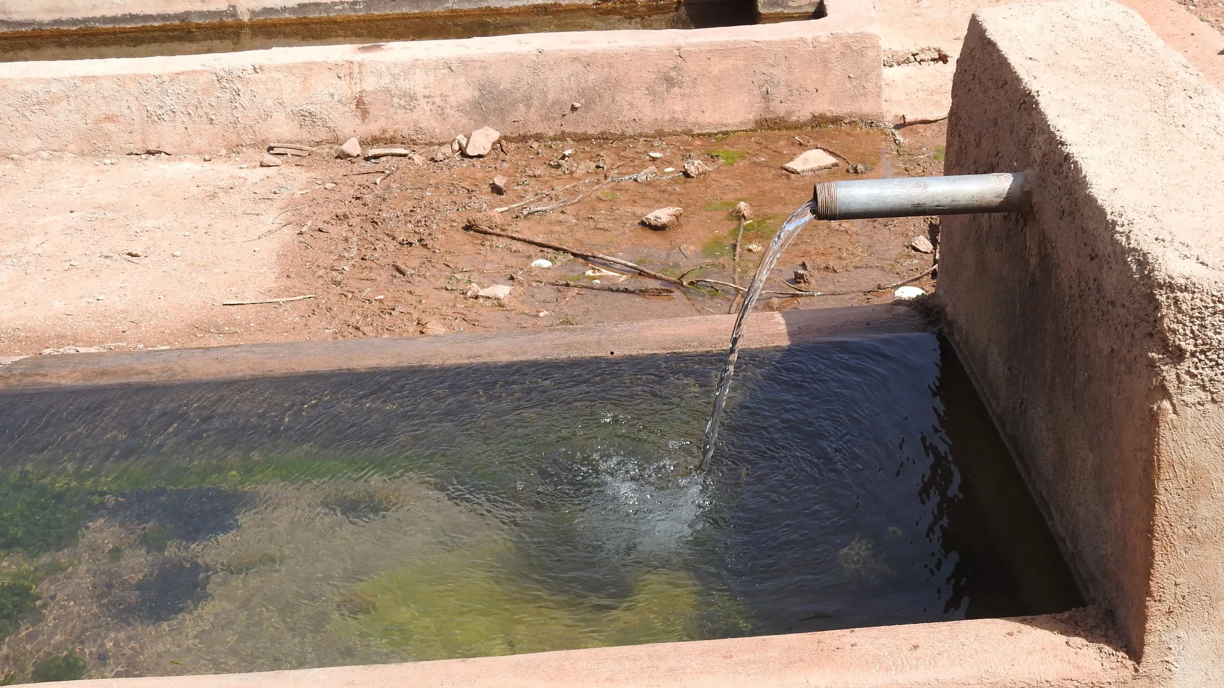 Water pouring from a metal pipe into a stone trough of clear water
