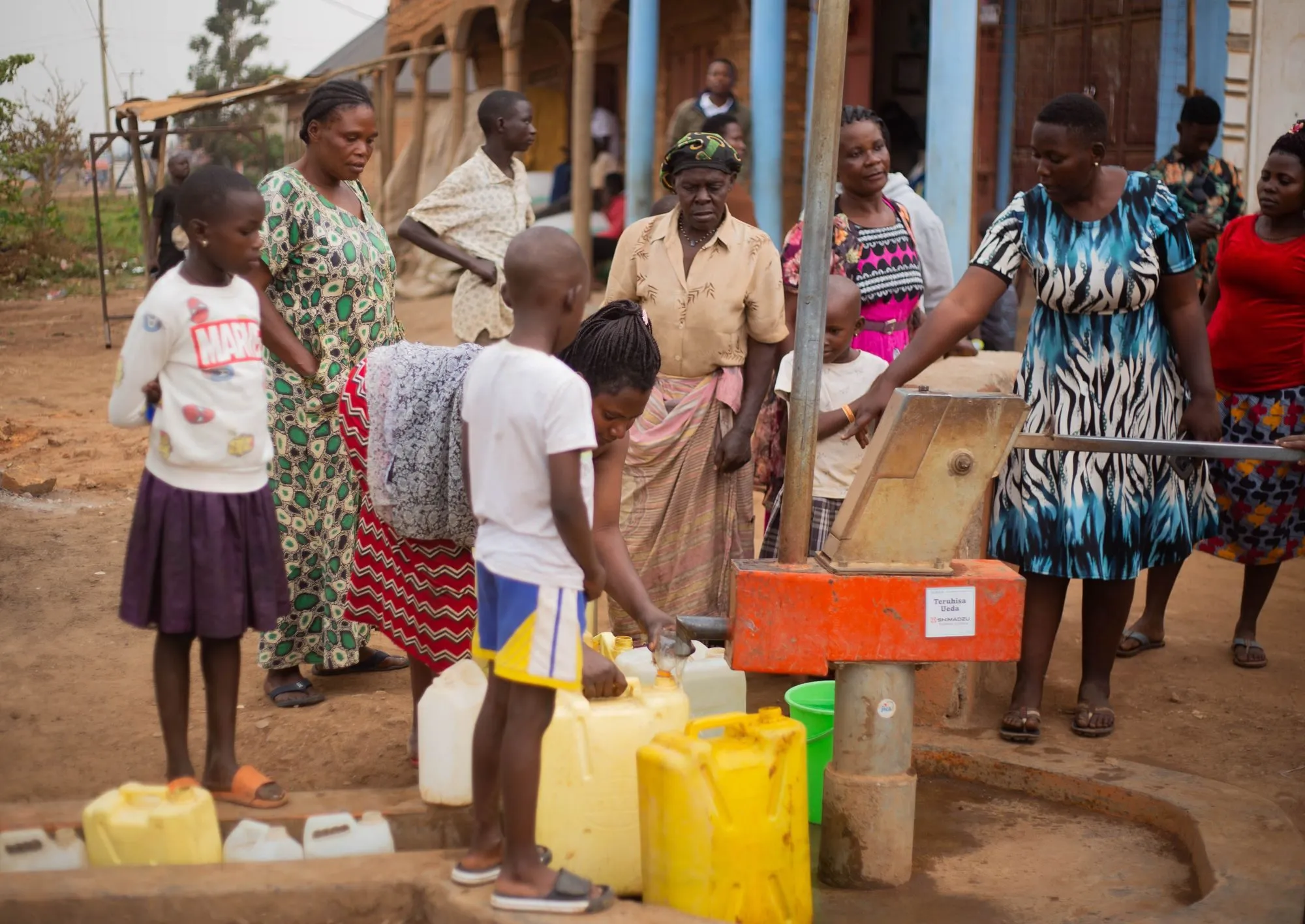 Women and children fill yellow jerrycans at a village water pump
