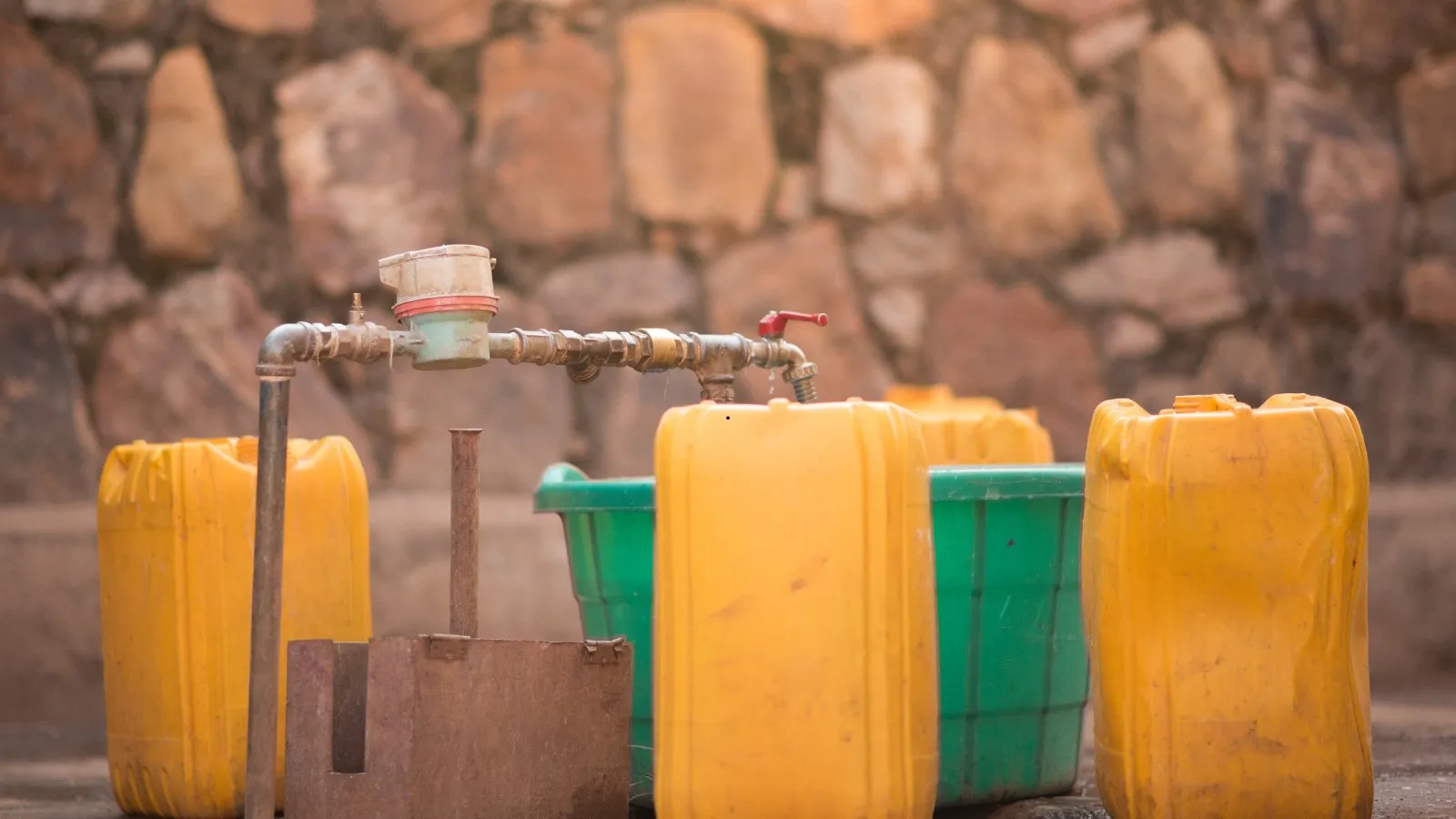 Yellow jerrycans and buckets lined up at a public water tap