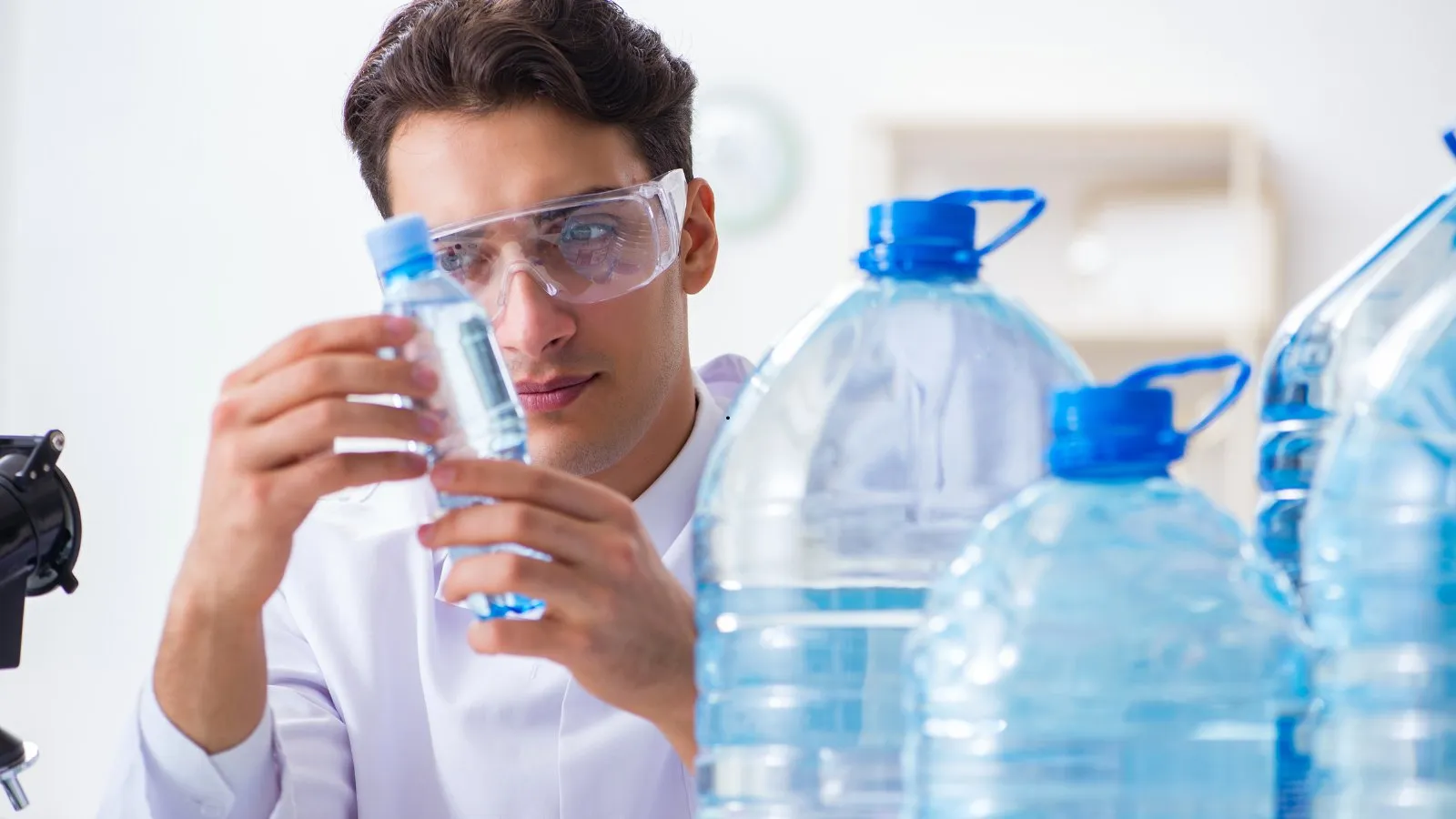 A laboratory worker in goggles holding up a bottle of drinking water to check it