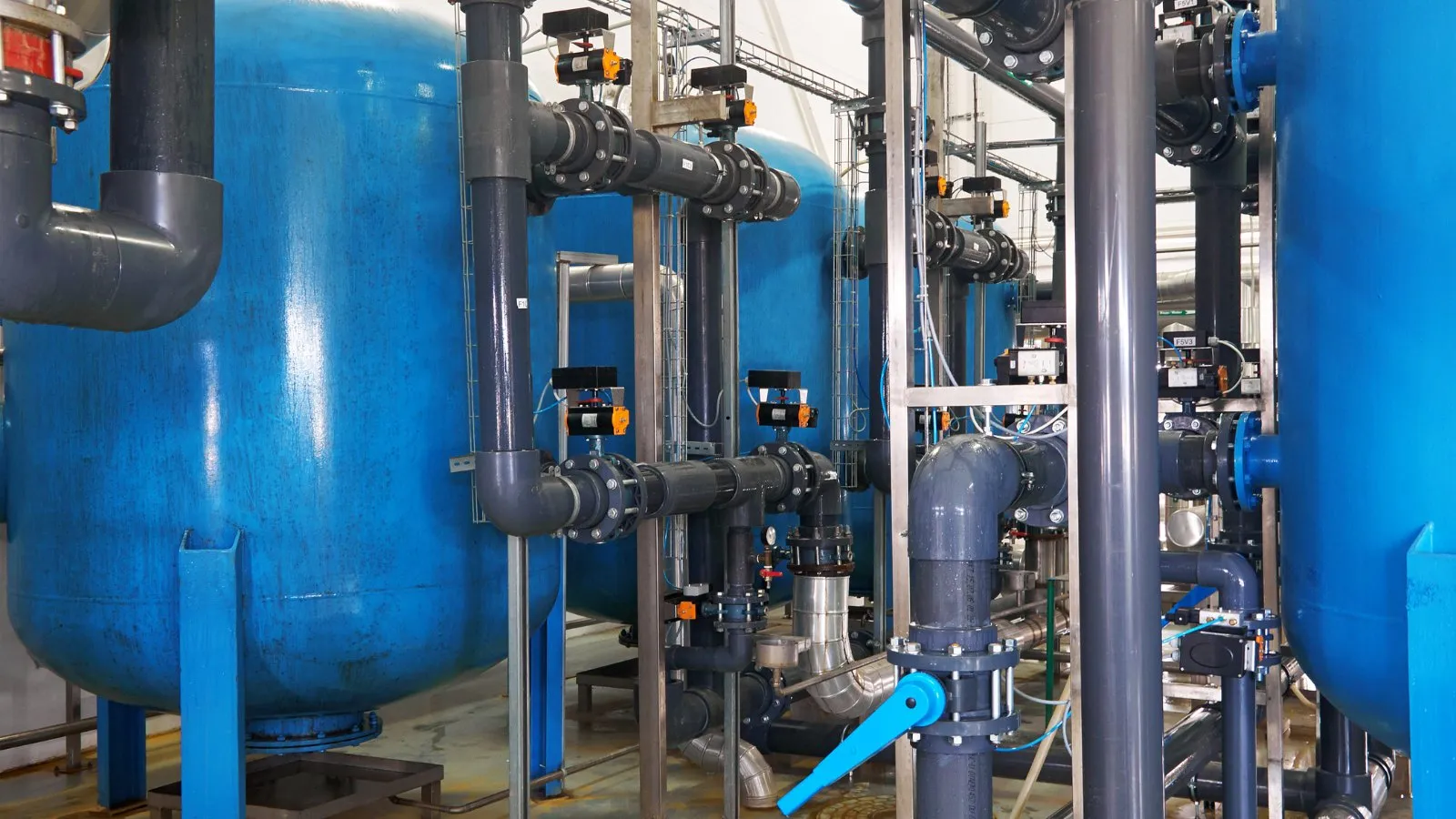 Blue filter vessels and grey pipework with valves inside a water treatment plant