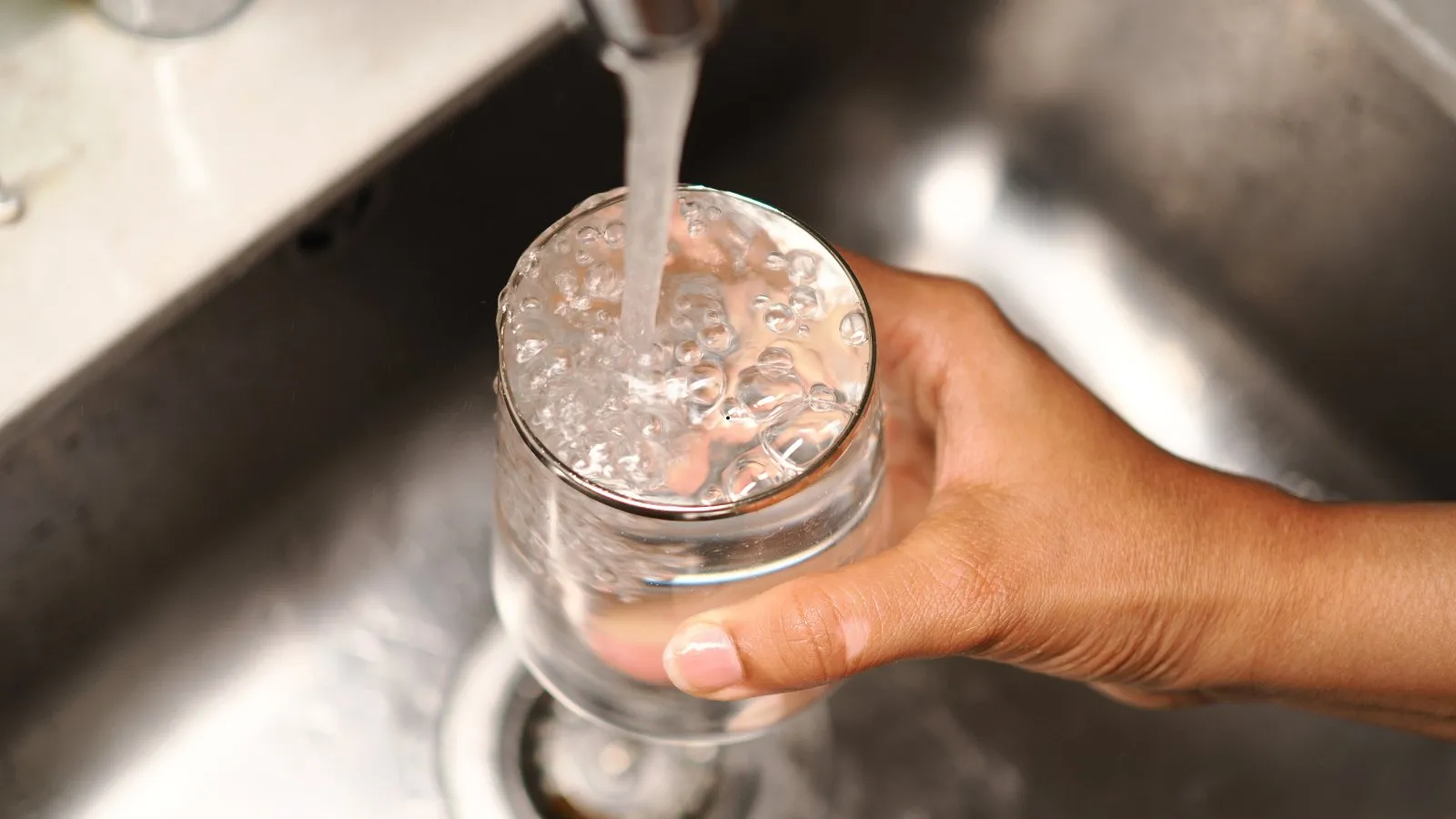 A hand holding a glass under a running kitchen tap