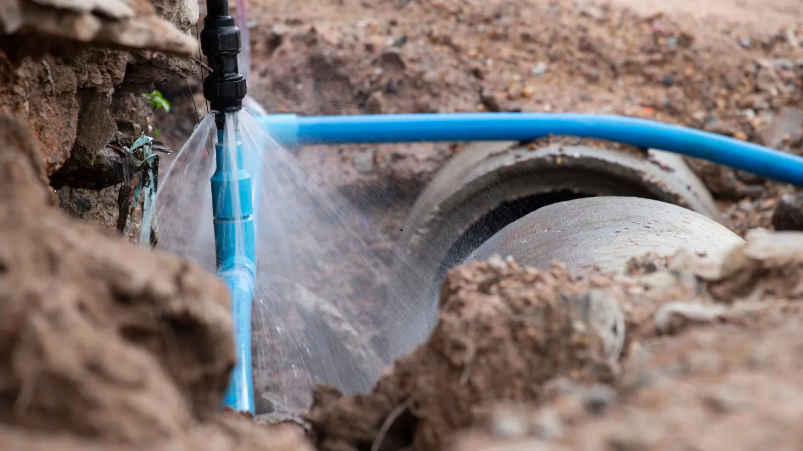 Water spraying from a burst main in a dug-out trench