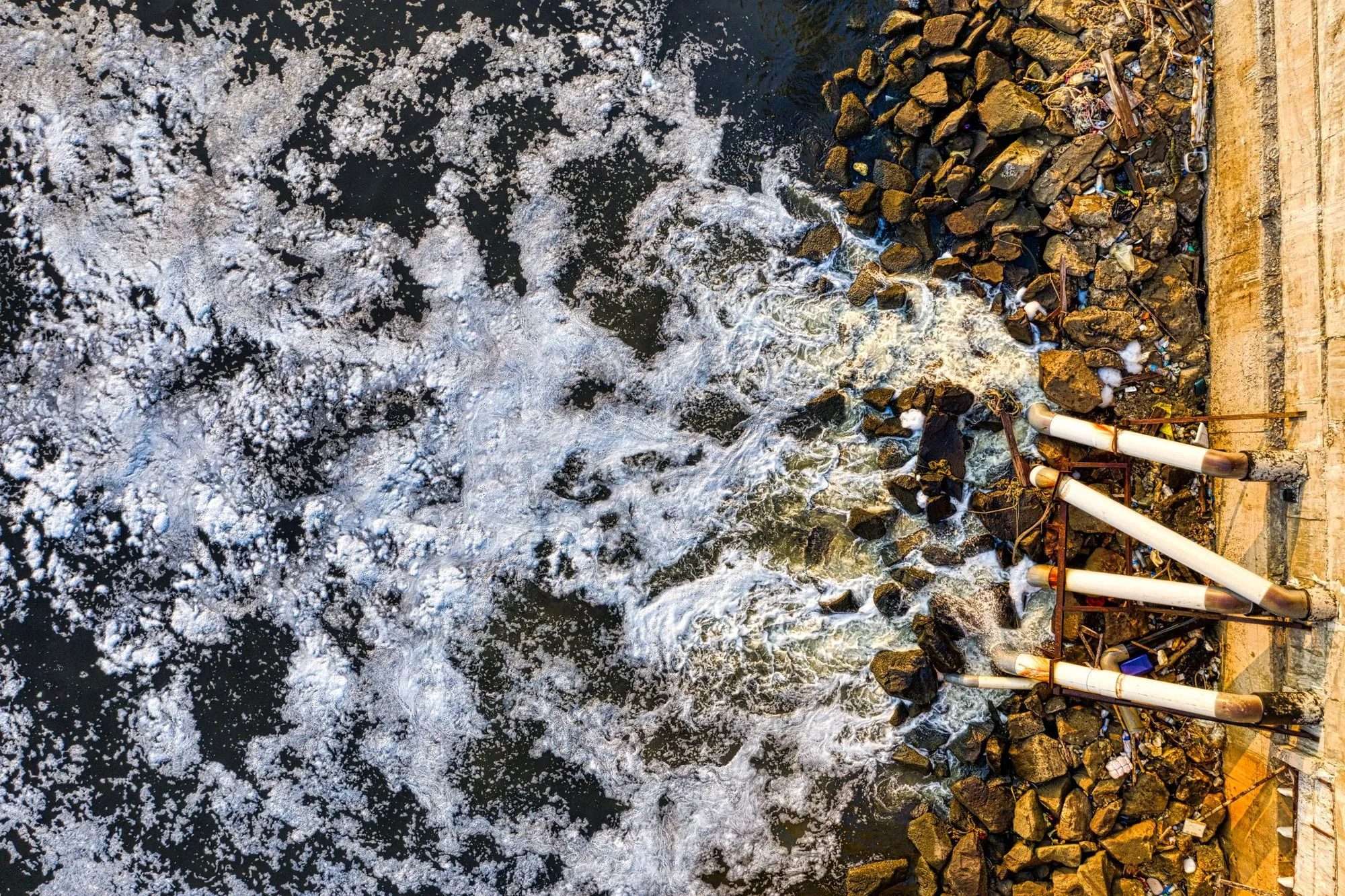 Pipes discharging dirty, foaming water into a river, seen from above
